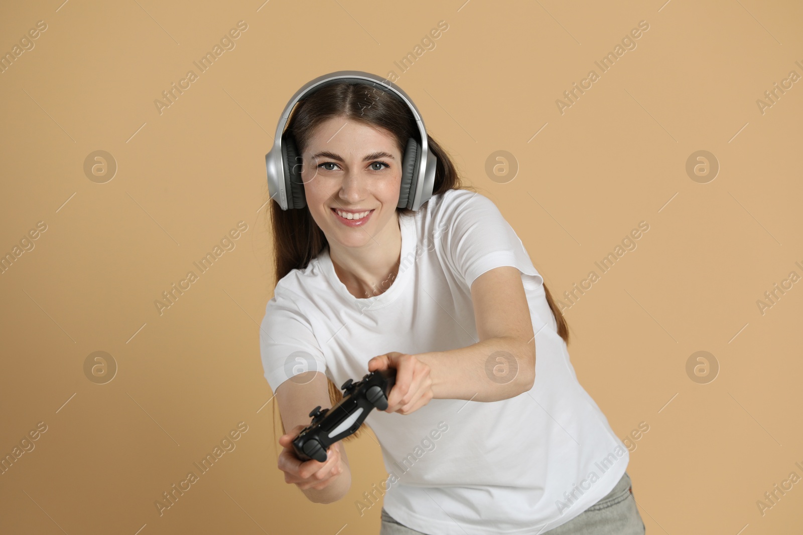 Photo of Happy woman in headphones playing video games with controller on beige background