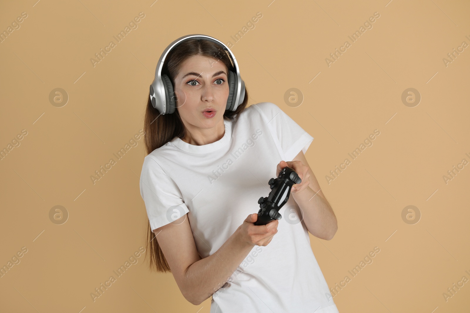 Photo of Woman in headphones playing video games with controller on beige background