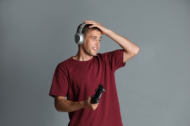 Emotional man in headphones with controller on gray background