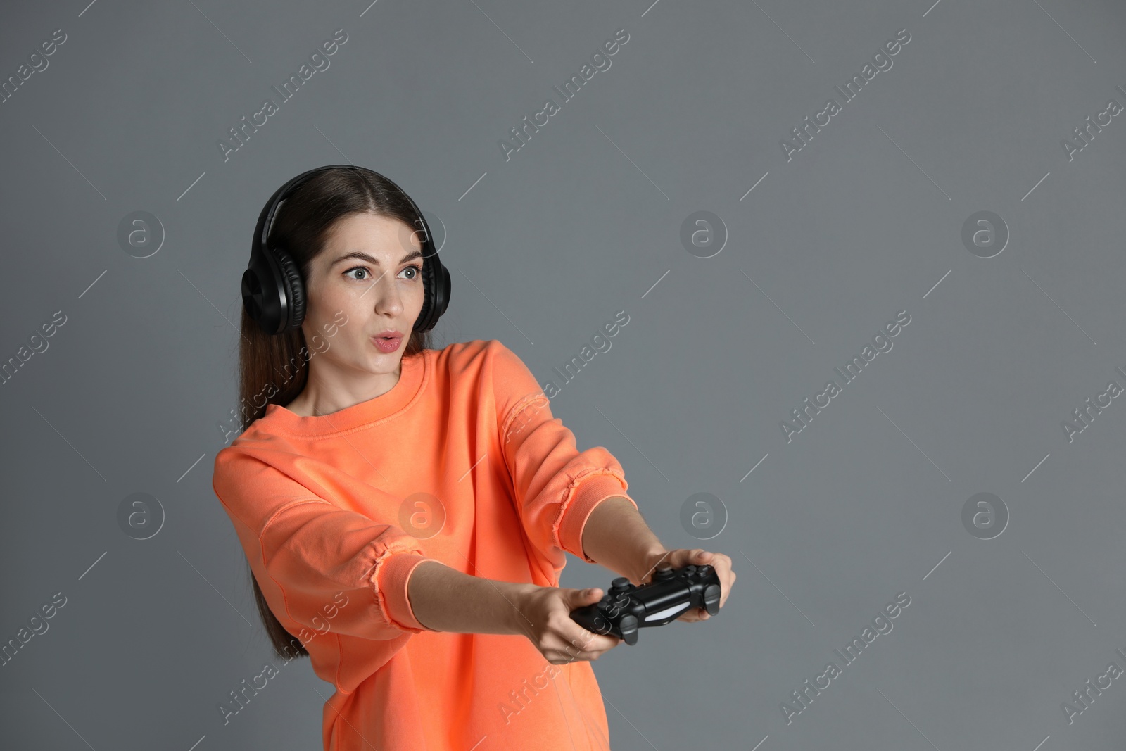 Photo of Surprised woman in headphones playing video games with controller on gray background, space for text