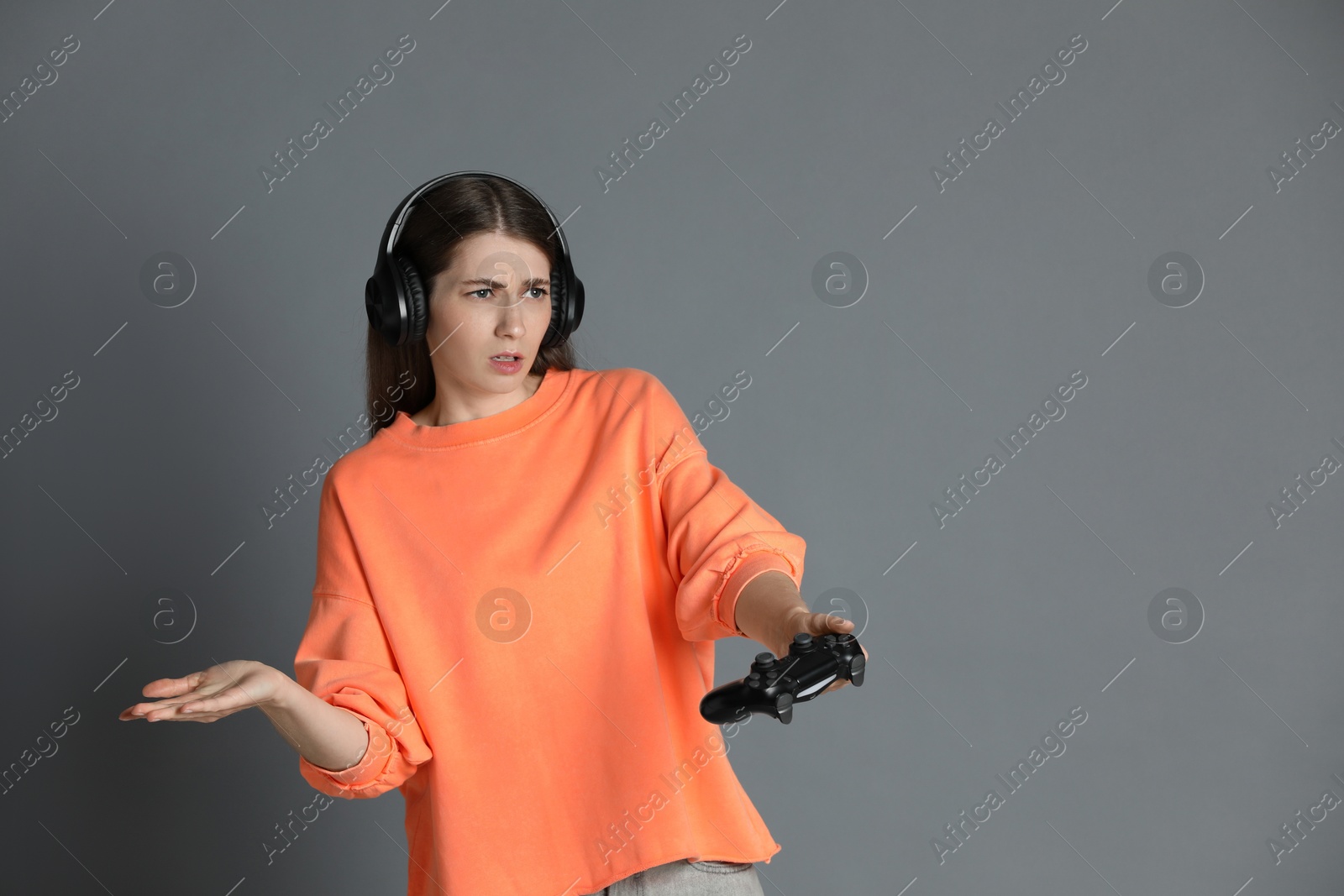 Photo of Woman in headphones playing video games with controller on gray background, space for text