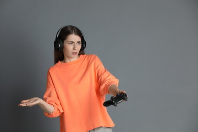 Woman in headphones playing video games with controller on gray background, space for text