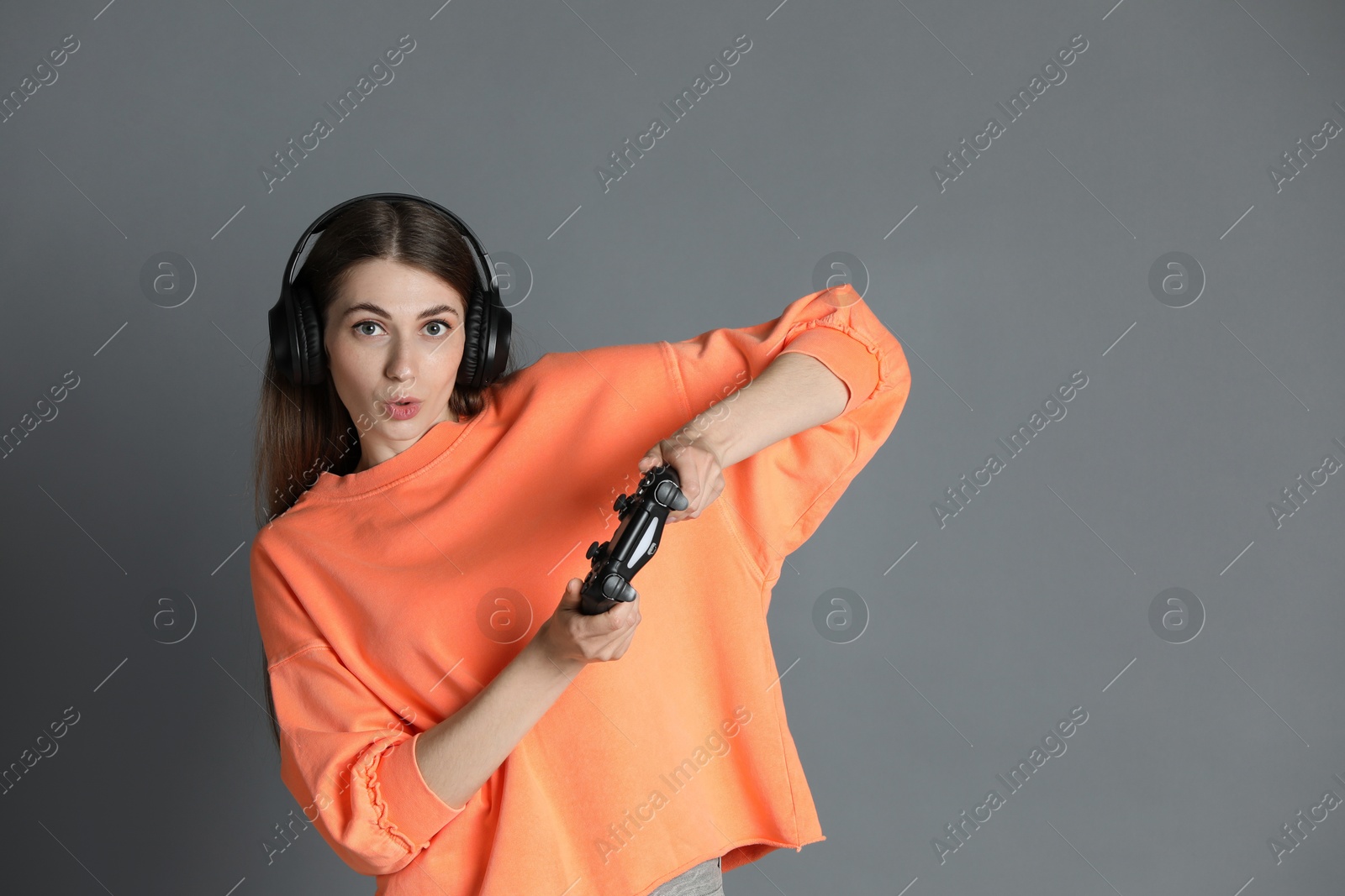 Photo of Surprised woman in headphones playing video games with controller on gray background, space for text