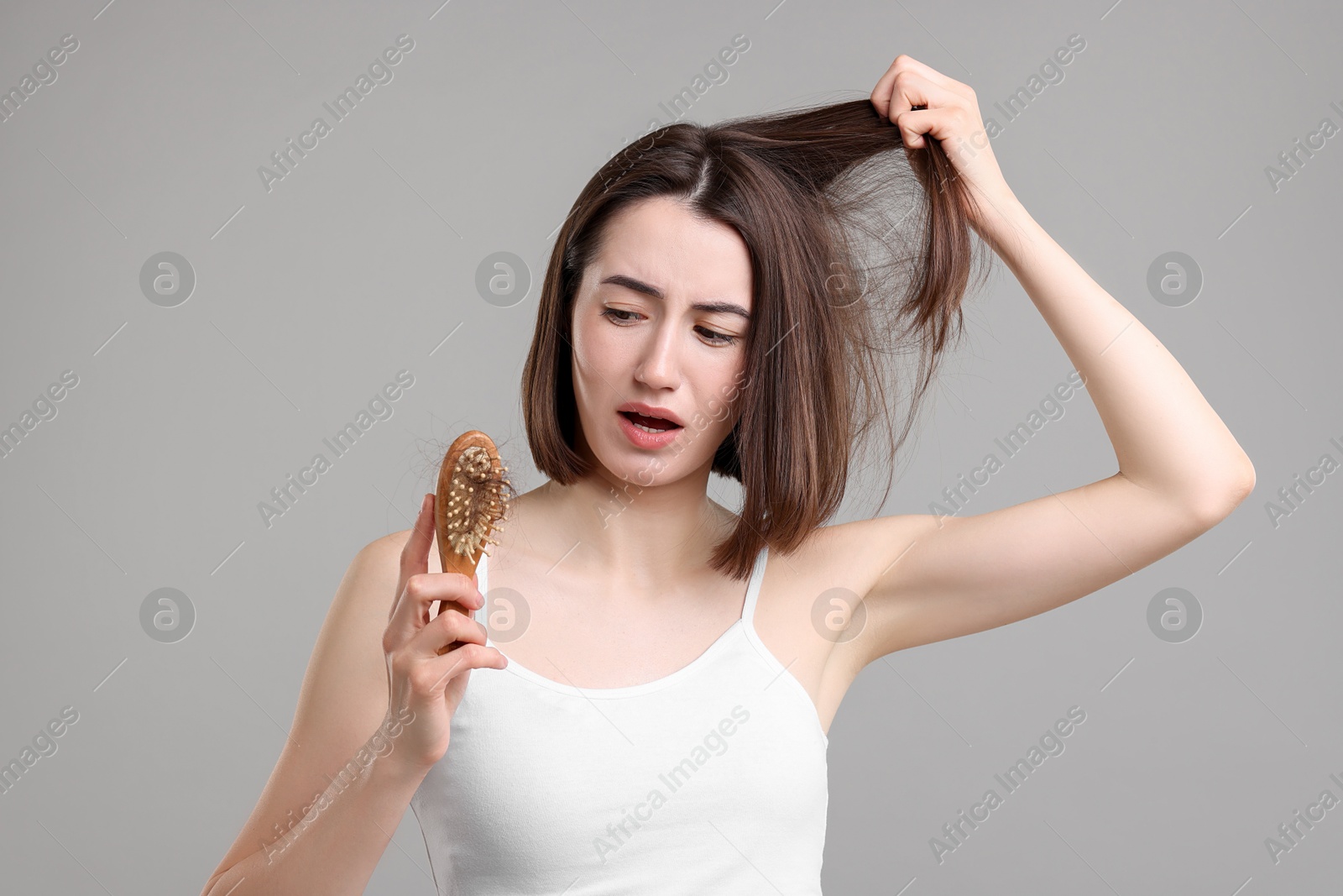 Photo of Sad woman holding brush with lost hair on grey background. Alopecia problem