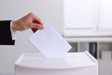 Photo of Woman putting her vote into ballot box indoors, closeup