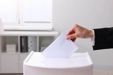 Photo of Woman putting her vote into ballot box indoors, closeup