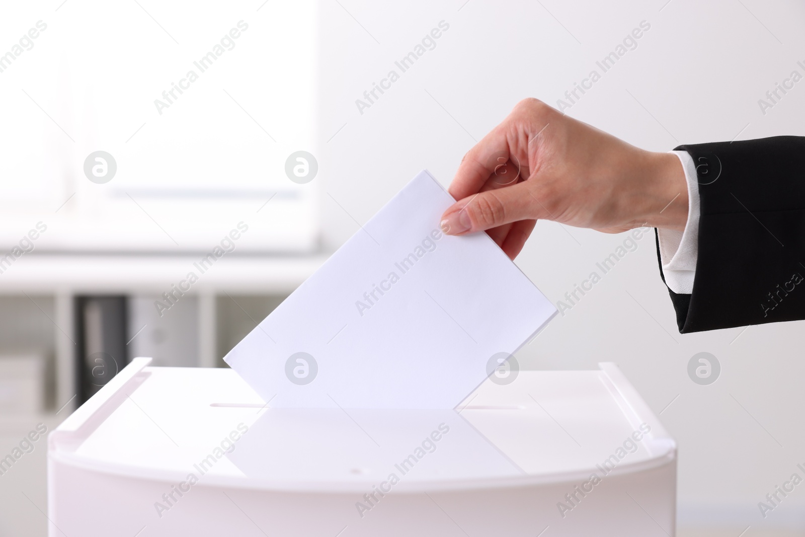 Photo of Woman putting her vote into ballot box indoors, closeup