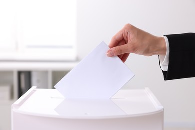 Woman putting her vote into ballot box indoors, closeup