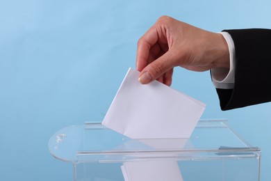 Photo of Woman putting her vote into ballot box against light blue background, closeup