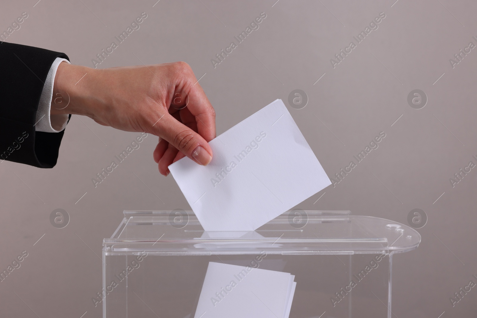 Photo of Woman putting her vote into ballot box against grey background, closeup