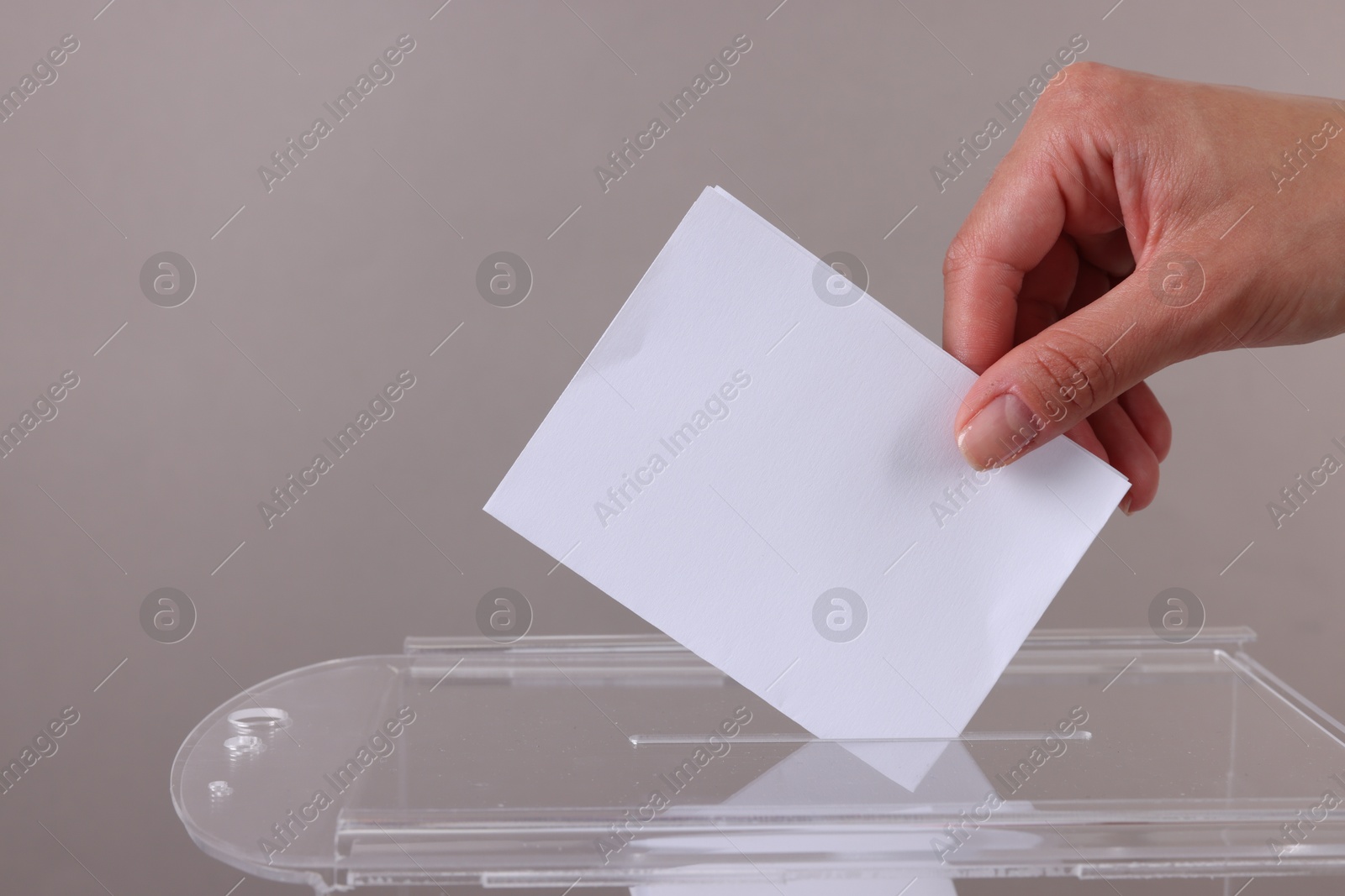 Photo of Woman putting her vote into ballot box against grey background, closeup