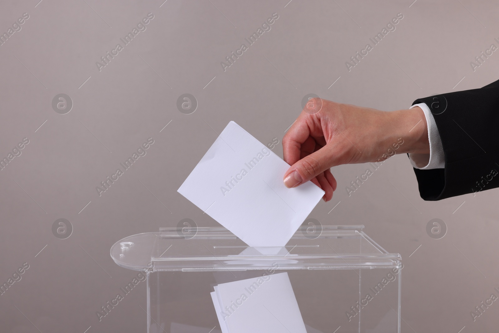 Photo of Woman putting her vote into ballot box against grey background, closeup