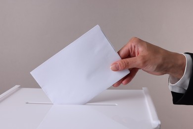 Woman putting her vote into ballot box against grey background, closeup