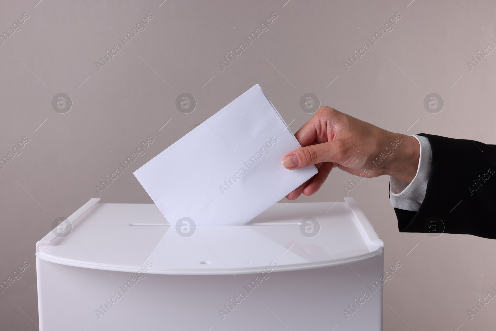 Photo of Woman putting her vote into ballot box against grey background, closeup