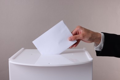 Woman putting her vote into ballot box against grey background, closeup