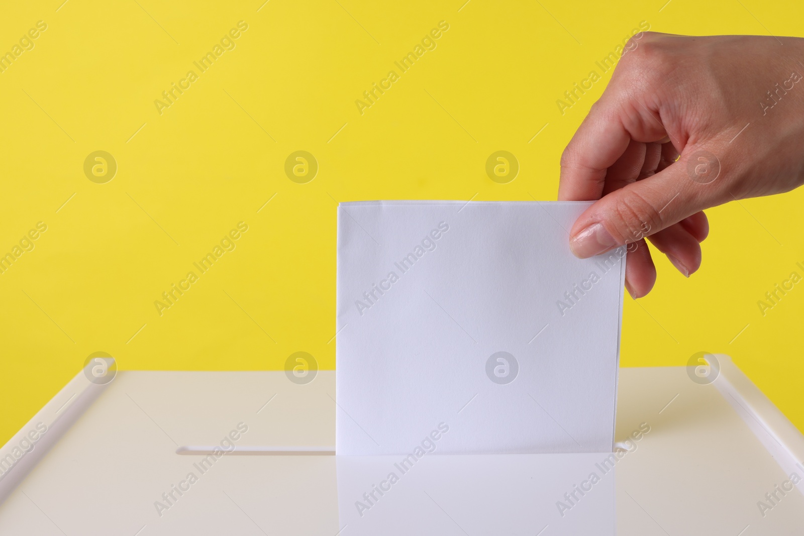 Photo of Woman putting her vote into ballot box against yellow background, closeup