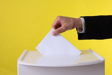 Photo of Woman putting her vote into ballot box against yellow background, closeup