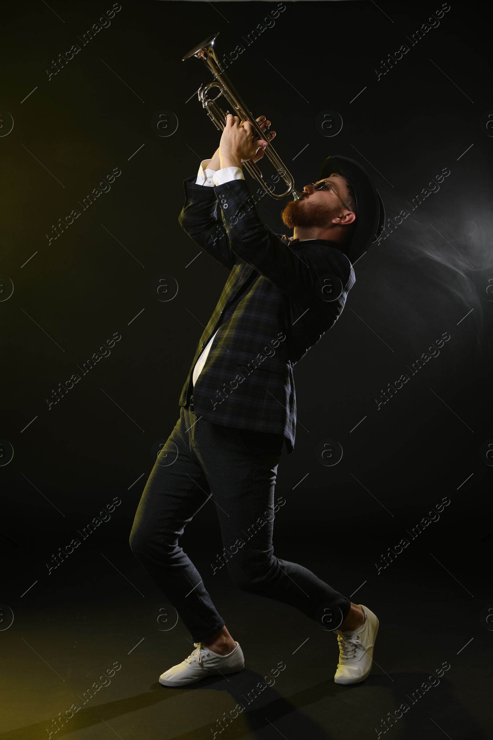 Photo of Professional musician playing trumpet on black background in color lights and smoke