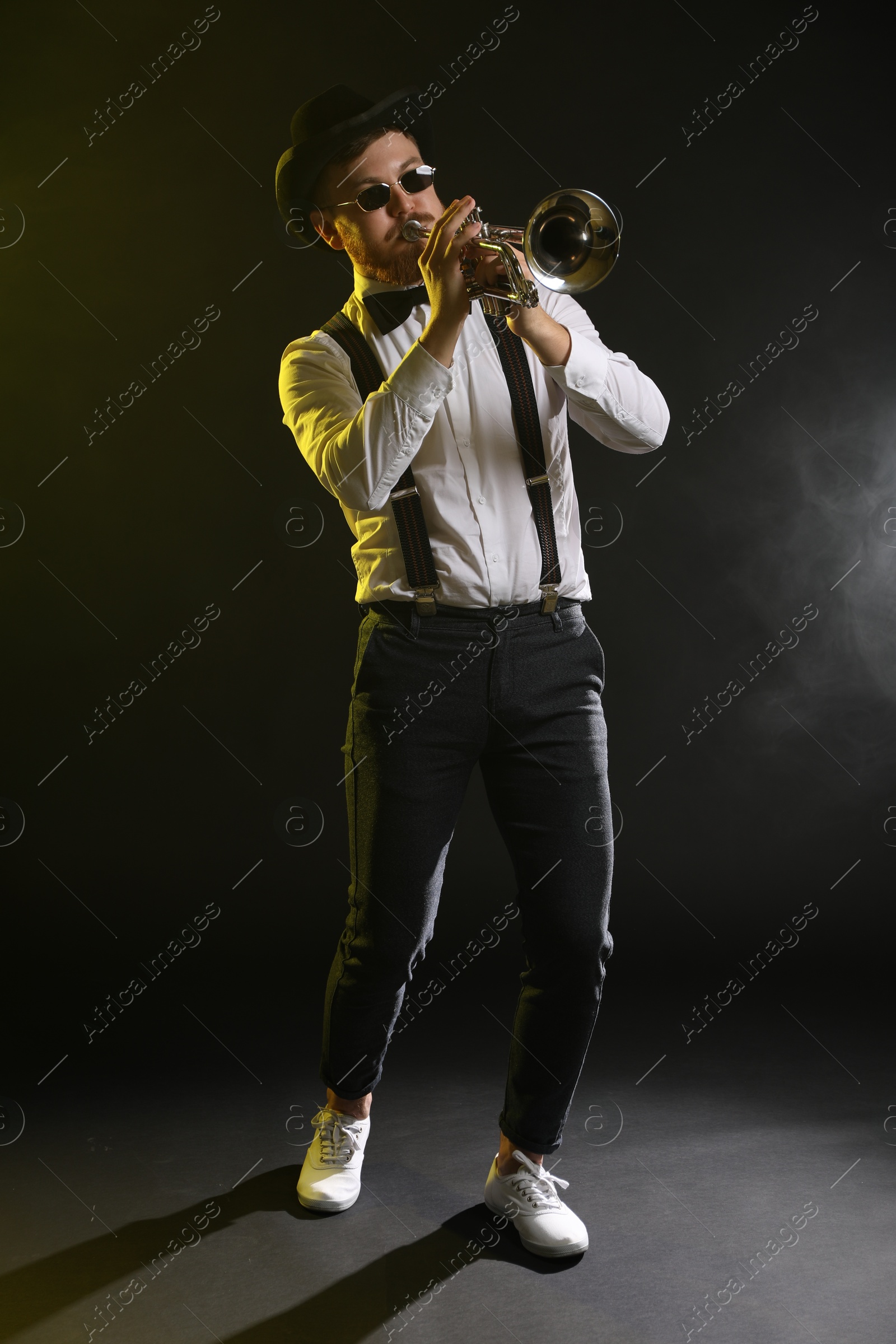 Photo of Professional musician playing trumpet on black background in color lights