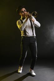 Professional musician playing trumpet on black background in color lights