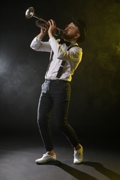 Professional musician playing trumpet on black background in color lights and smoke