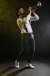 Photo of Professional musician playing trumpet on black background in color lights and smoke