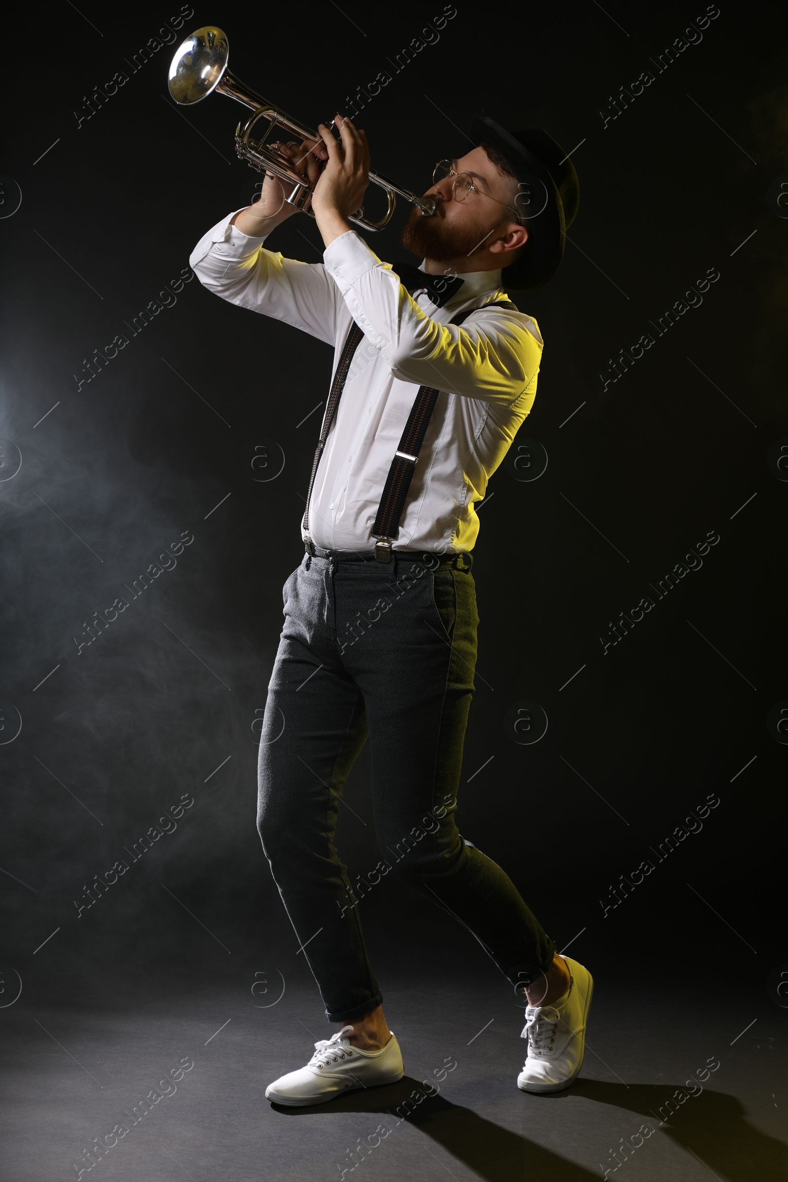 Photo of Professional musician playing trumpet on black background in color lights and smoke