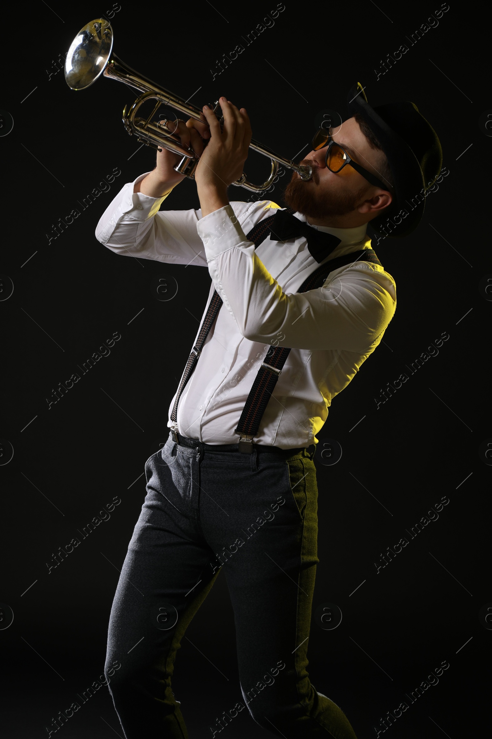 Photo of Professional musician playing trumpet on black background in color lights