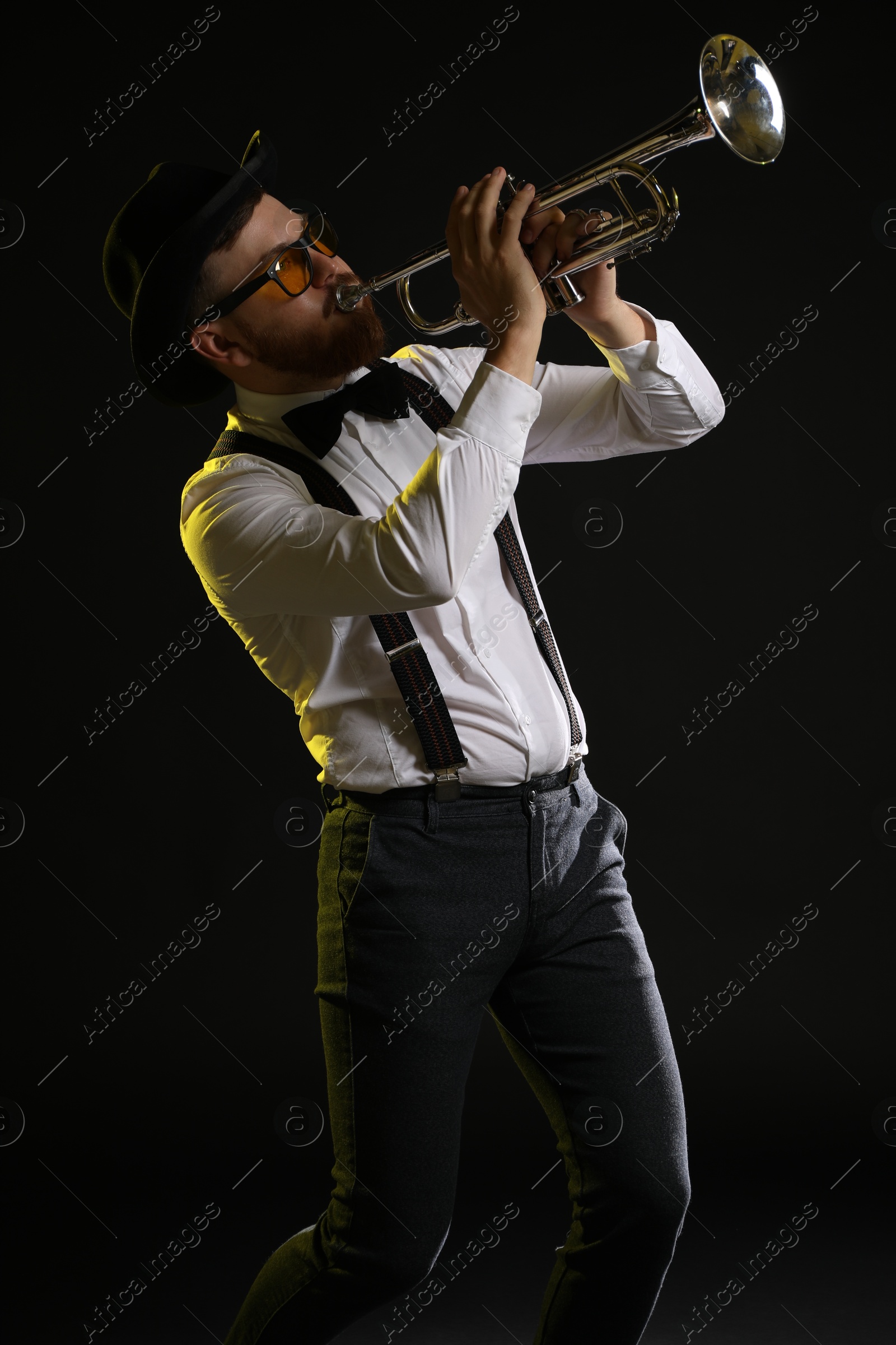 Photo of Professional musician playing trumpet on black background in color lights