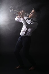 Professional musician playing trumpet on black background with smoke