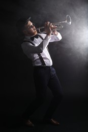 Photo of Professional musician playing trumpet on black background with smoke