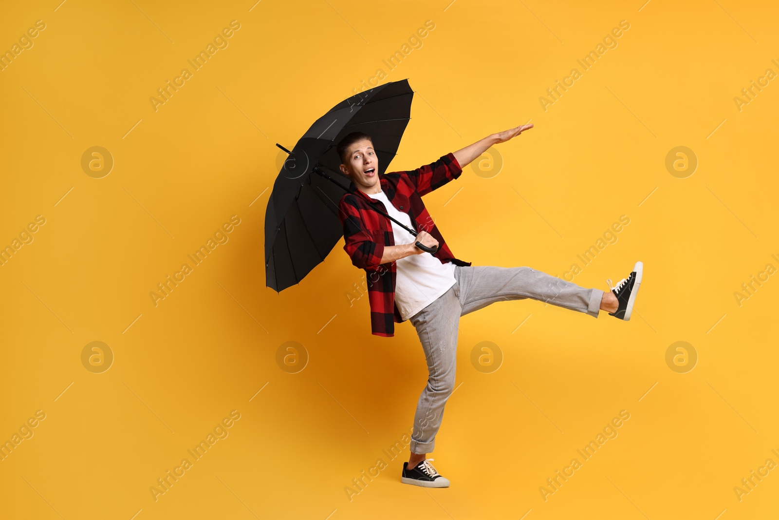 Photo of Young man with black umbrella on yellow background