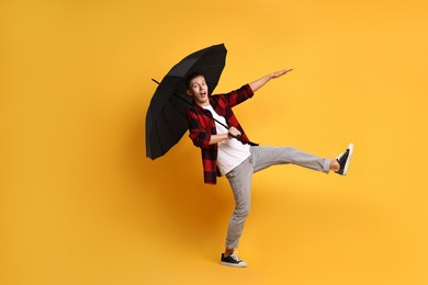 Photo of Young man with black umbrella on yellow background