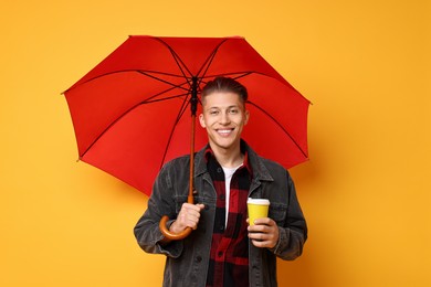 Photo of Young man with red umbrella and cup of drink on yellow background