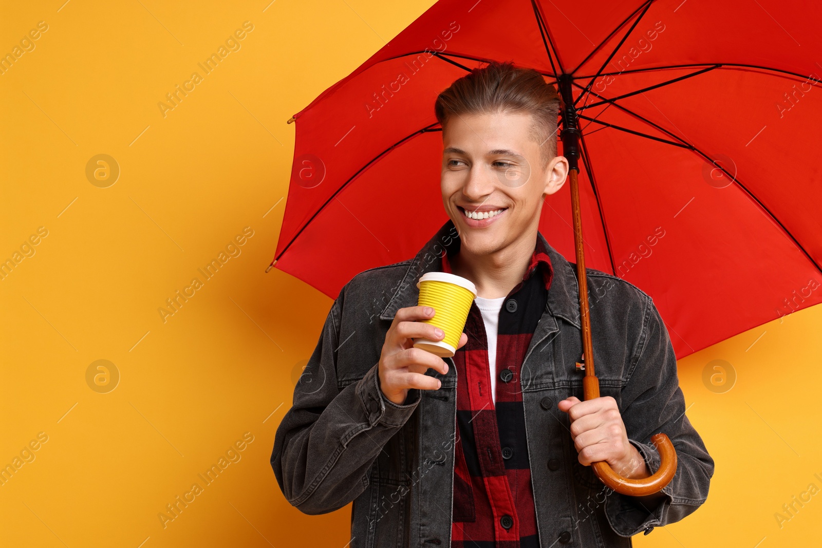 Photo of Young man with red umbrella and cup of drink on yellow background, space for text