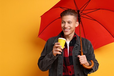 Young man with red umbrella and cup of drink on yellow background, space for text