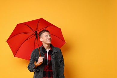 Photo of Young man with red umbrella on yellow background, space for text