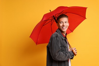 Young man with red umbrella on yellow background