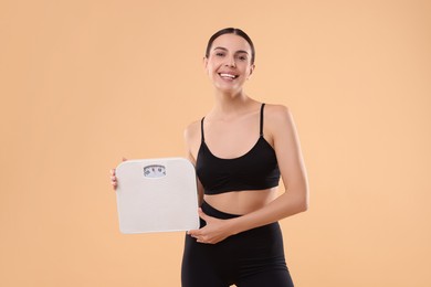 Photo of Diet and weight loss concept. Happy young woman with floor scale on beige background