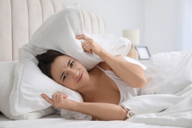 Woman covering ears with pillow in bed at home