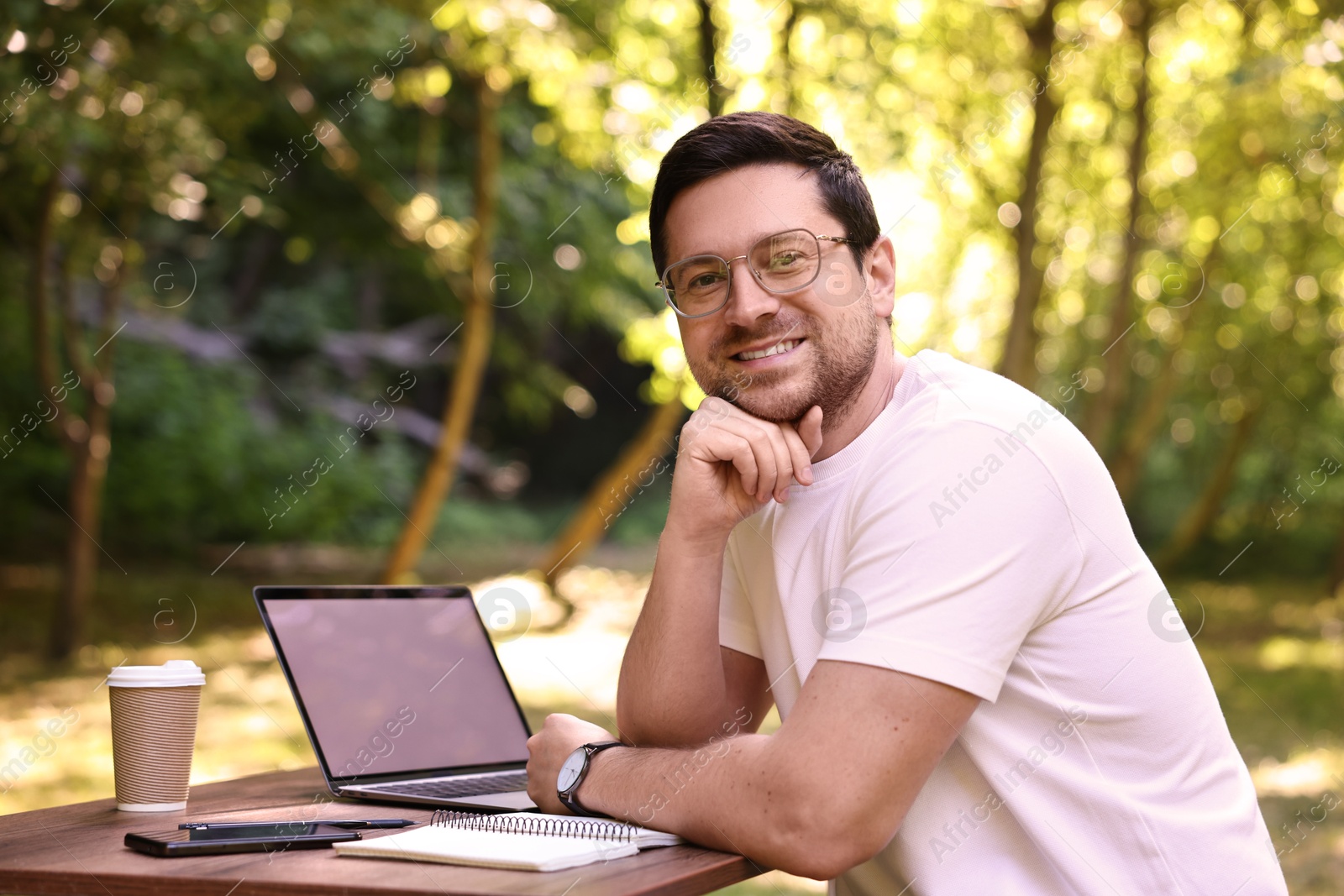 Photo of Smiling freelancer sitting at table with laptop outdoors. Remote work