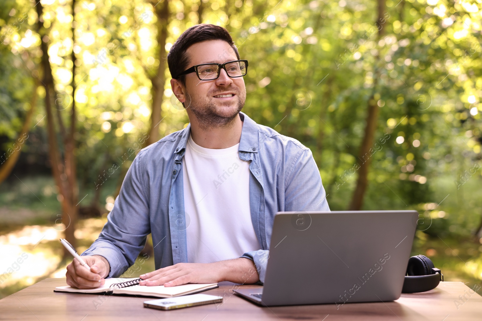 Photo of Smiling freelancer working with laptop and writing something at table outdoors. Remote job