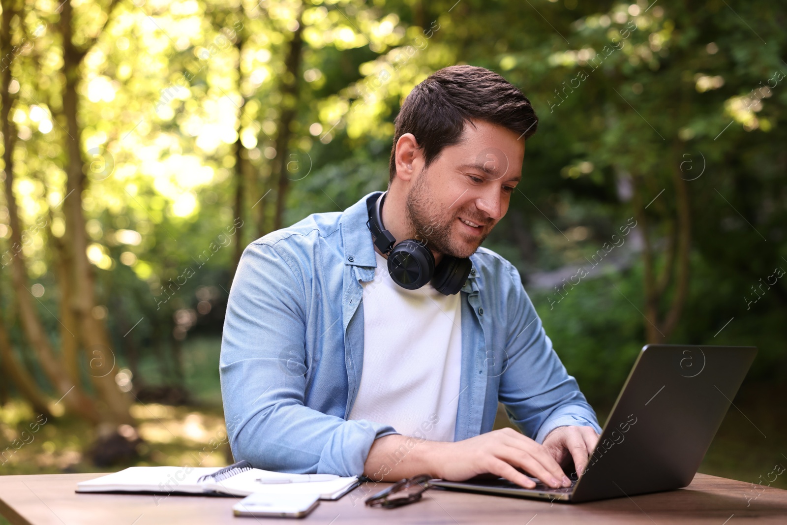 Photo of Smiling freelancer working with laptop at table outdoors. Remote job