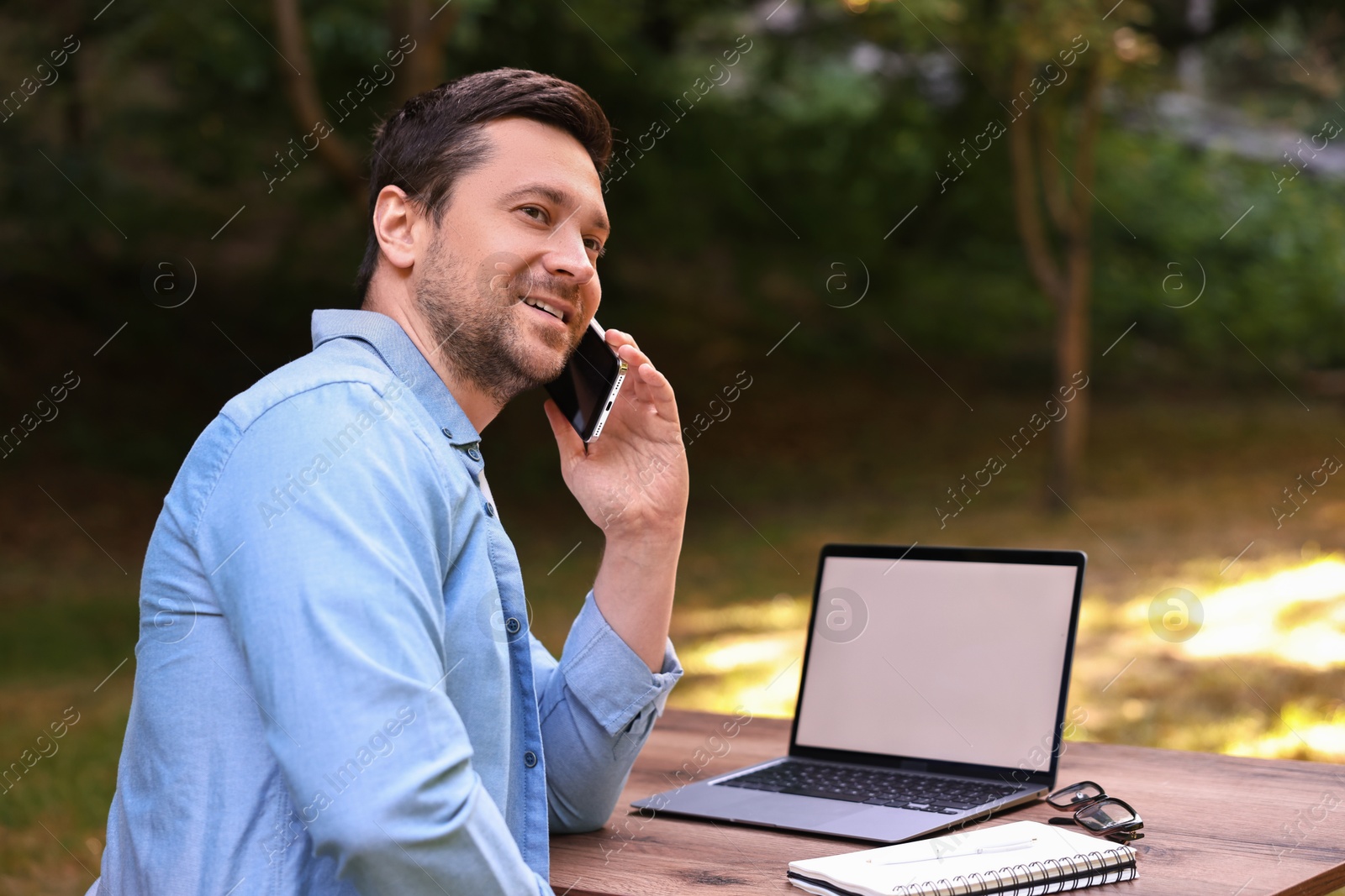 Photo of Smiling freelancer talking on smartphone outdoors. Remote job