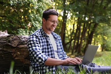 Photo of Smiling freelancer working with laptop on green grass in forest. Remote job