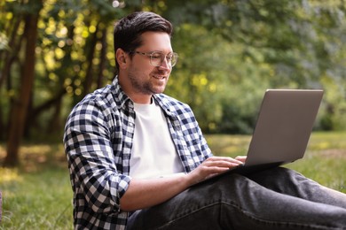 Photo of Smiling freelancer working with laptop in forest. Remote job