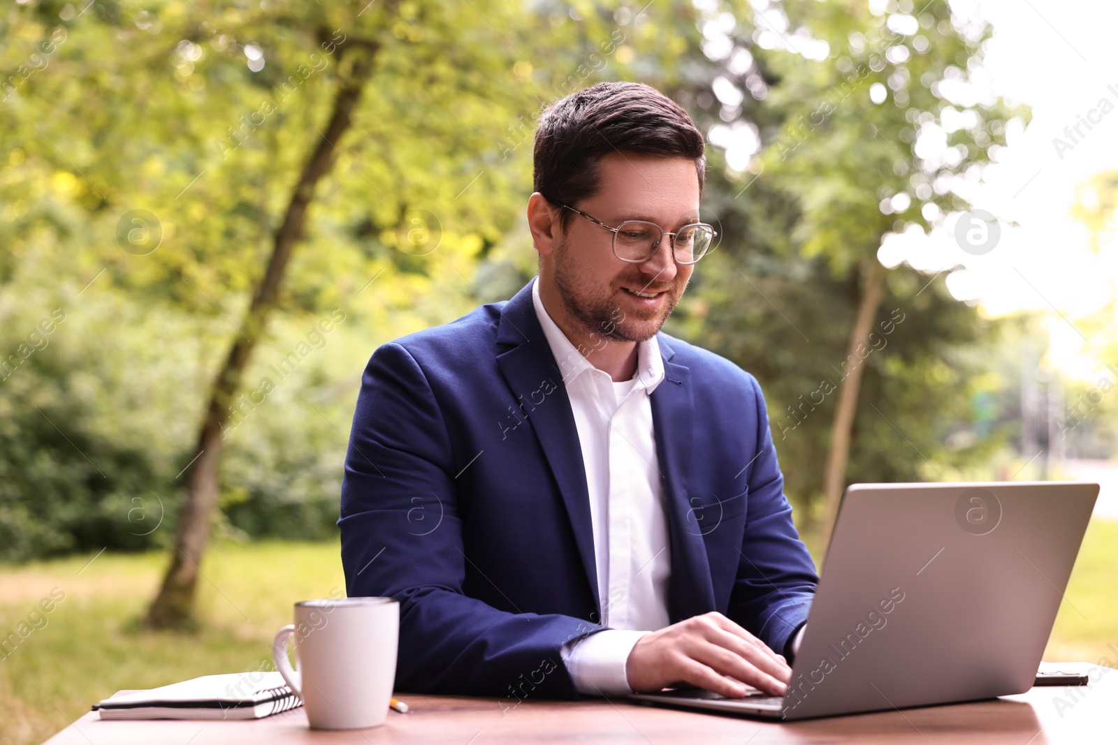 Photo of Smiling businessman working with laptop at table outdoors. Remote job