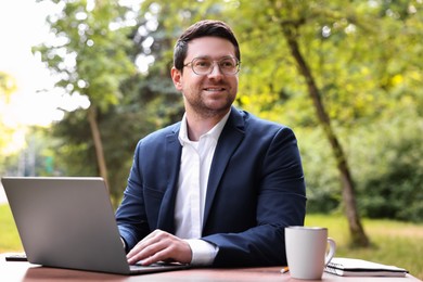 Smiling businessman working with laptop at table outdoors. Remote job