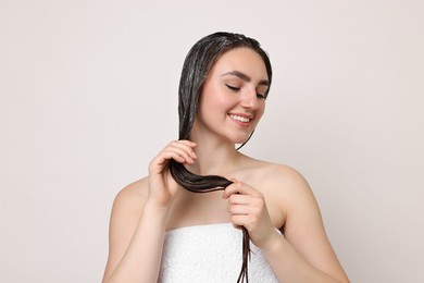 Smiling woman applying hair mask on light background