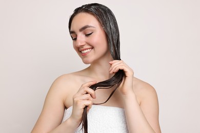 Photo of Smiling woman applying hair mask on light background